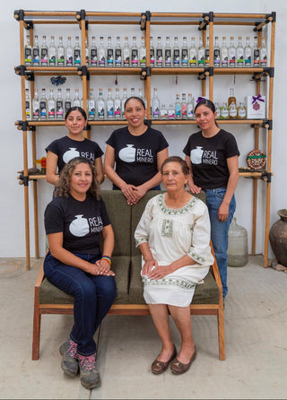 The five Angeles women sitting in front of shelves of Real Minero mezcal bottles